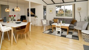 A modern living room with a dining area, featuring a large window, wooden flooring, and contemporary furniture. - 6 Person Holiday Home in Olsted (Frederiksvaerk)