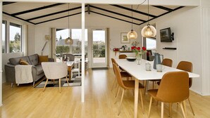 A modern dining area with a white table and brown chairs, a sofa, and a large window with a view. - 6 Person Holiday Home in Olsted (Frederiksvaerk)