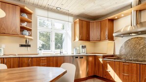 A modern kitchen with wooden cabinets, a granite countertop, and a built-in dishwasher. - 4 Star Holiday Home in Vaeggerlose (Vaeggerlose)