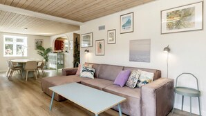 A cozy living room with a wooden ceiling, a beige sofa, a light-colored coffee table, and a dining area with a wooden table and chairs. - 4 Star Holiday Home in Vaeggerlose (Vaeggerlose)