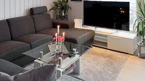 Un salon moderne avec un canapé d’angle, une table basse en verre, un téléviseur à écran plat et une grande fenêtre.