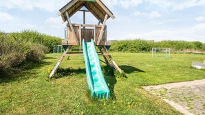 A wooden playhouse with a slide in a grassy area. - 5 Star Holiday Home in Lokken (Lokken)