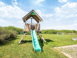 A wooden playhouse with a slide in a grassy area. - 5 Star Holiday Home in Lokken (Lokken)