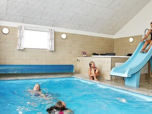 Una piscina interior con tobogán, un banco y una ventana.
