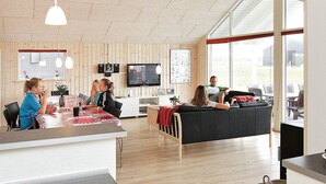 A modern interior with a wooden floor, a dining area with a table and chairs, a black sofa, and a television mounted on the wall. - 5 Star Holiday Home in Lokken (Lokken)