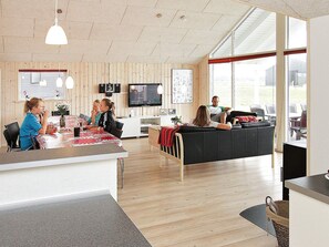 A modern interior with a wooden floor, a dining area with a table and chairs, a black sofa, and a television mounted on the wall. - 5 Star Holiday Home in Lokken (Lokken)
