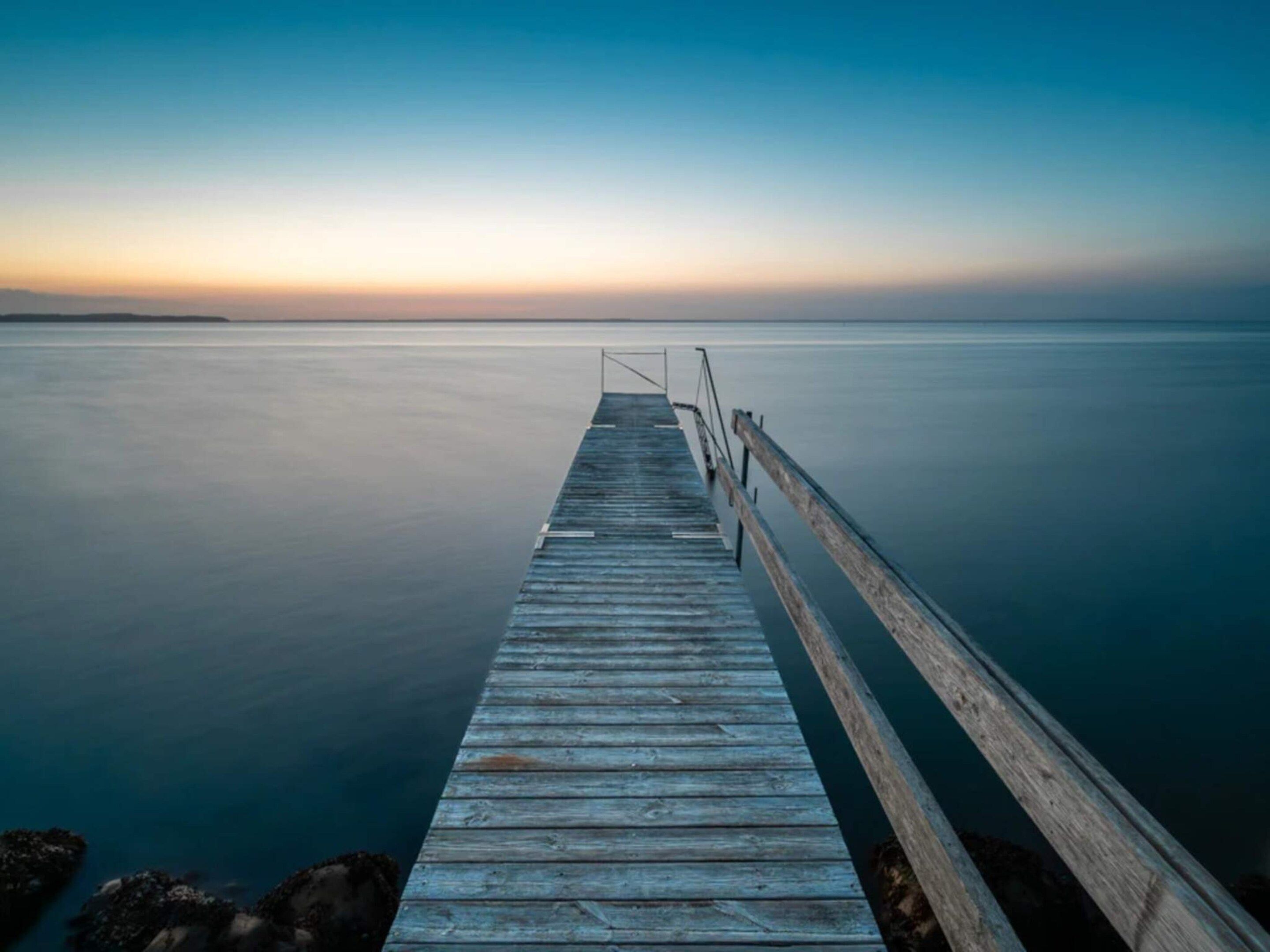 A wooden pier extending into calm water, with a metal railing on one side.