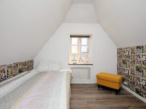 A bedroom with a sloped ceiling, a bed with a patterned bedspread, a window with a view, and comic book wallpaper on the walls. - 7 Person Holiday Home in Bogense (Bogense)