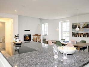 A modern kitchen with a central island, a dining area with a table and chairs, a fireplace, and a large window. - 7 Person Holiday Home in Bogense (Bogense)