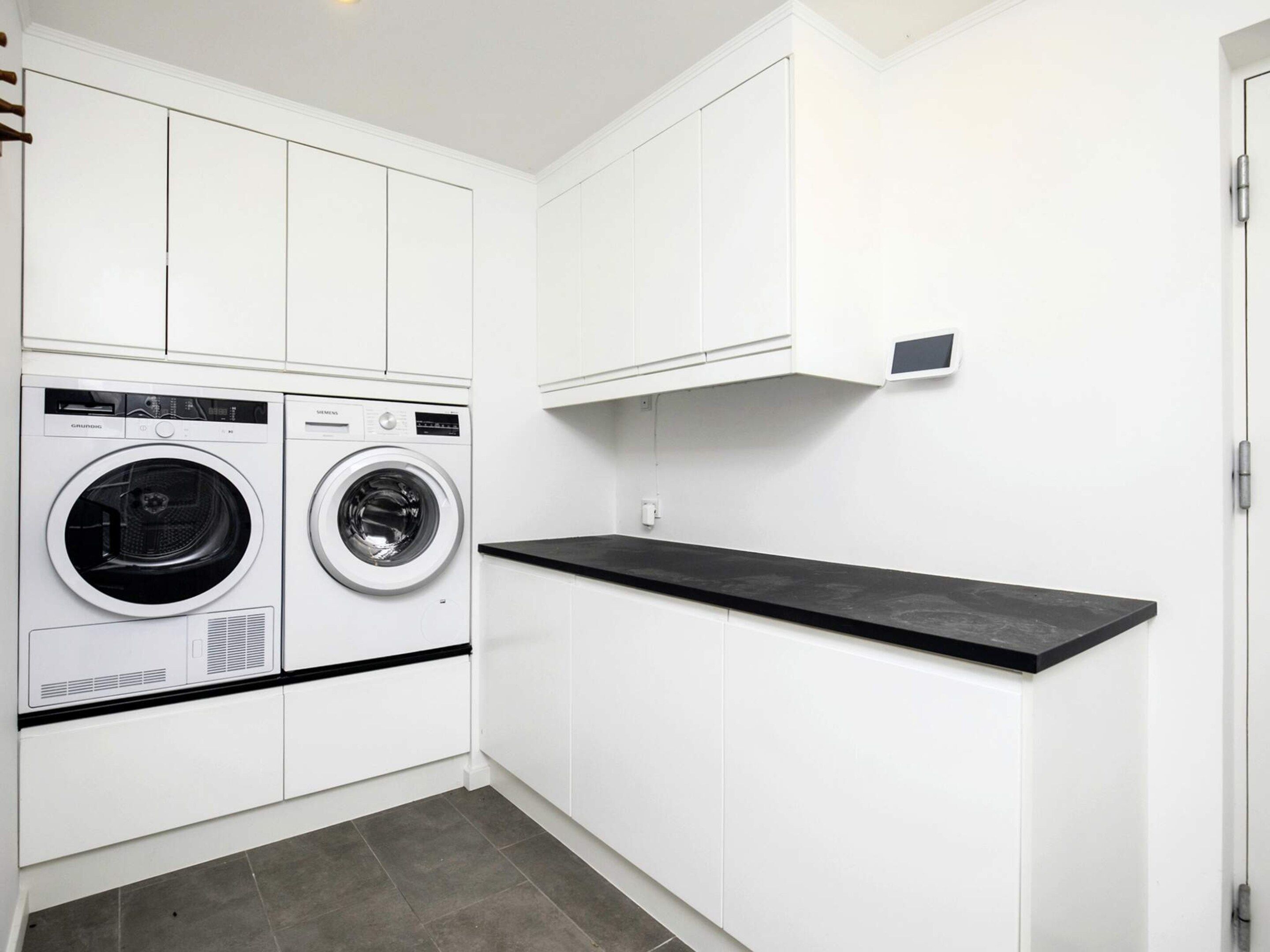 A compact laundry room with two front-loading washing machines, white cabinetry, and a black countertop.