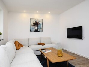 A modern living room with a sectional sofa, a coffee table, a painting, and a flat-screen TV.