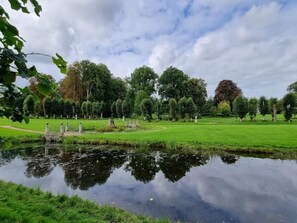 Un parco tranquillo con uno stagno, vialetti e alberi curati.
