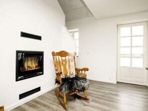 A room with a fireplace, a rocking chair, and a large window. - 7 Person Holiday Home in Bogense (Bogense)