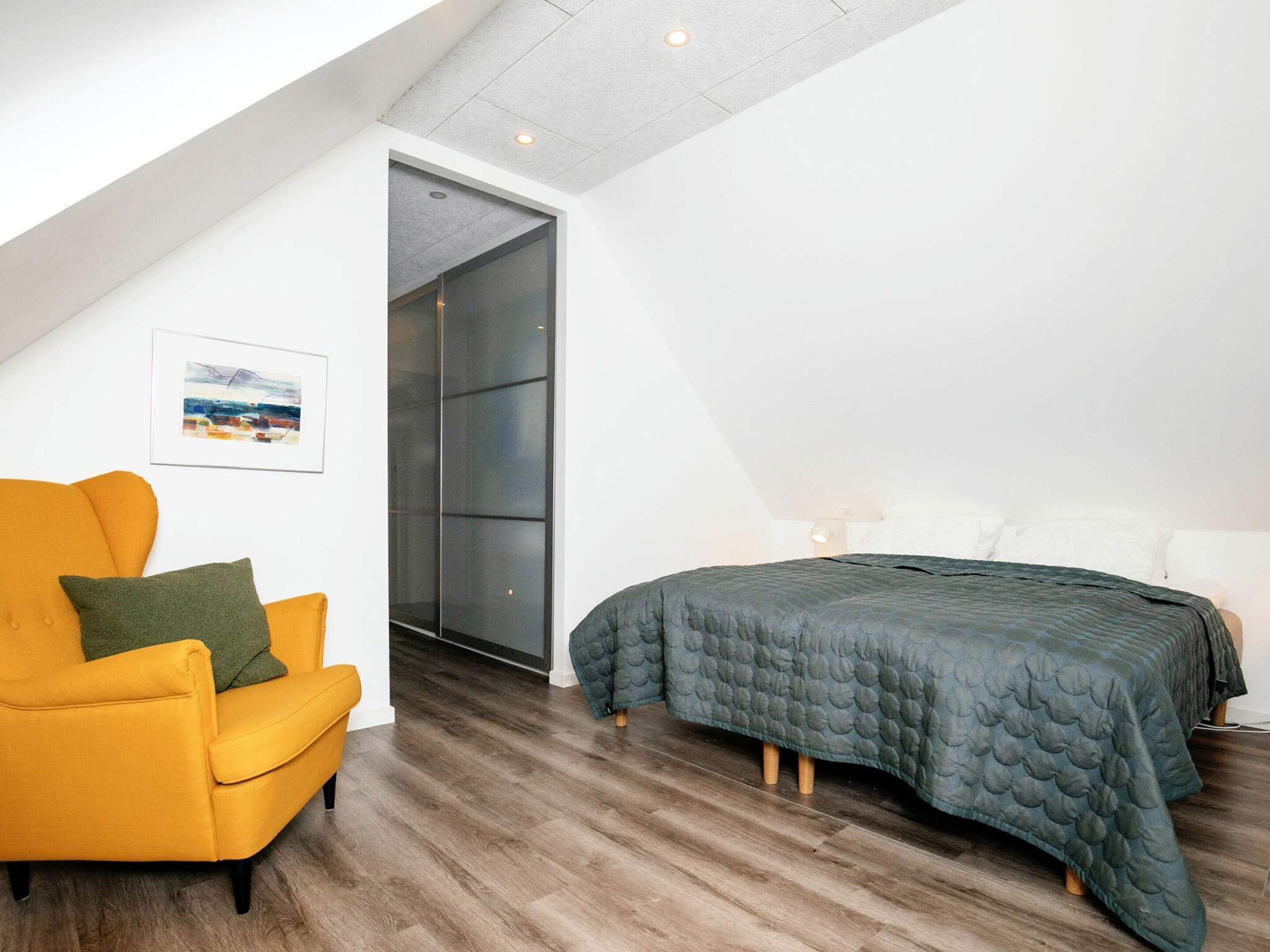 A bedroom with a bed, a chair, and a door leading to a balcony.