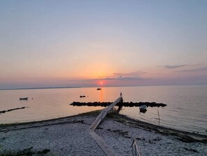 A sunset view over a calm sea with a wooden walkway leading to the water.