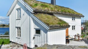 A white building with a grass roof, a wooden door, and a small outdoor seating area. - 7 Person Holiday Home in Averoy (Averoy)
