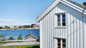 A white building with a small window and a door, located near a body of water with houses in the background. - 7 Person Holiday Home in Averoy (Averoy)