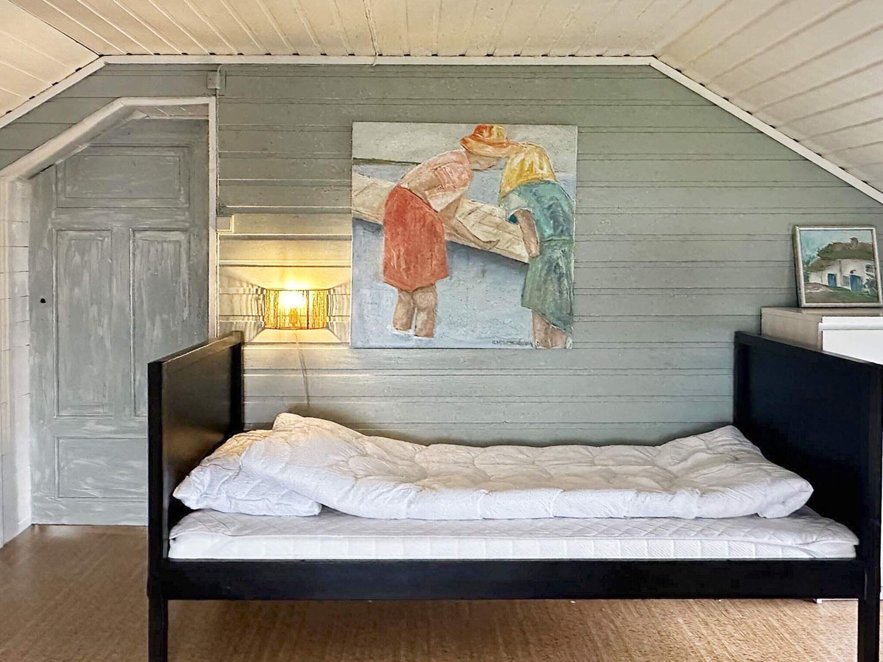 A bedroom with a bed, a painting on the wall, and a door.