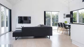 En moderne stue med sofa, fladskærms-tv, spiseplads med stole og store vinduer.
