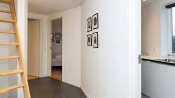 A hallway with a wooden ladder, a kitchen area with a window, and a door leading to a bedroom.