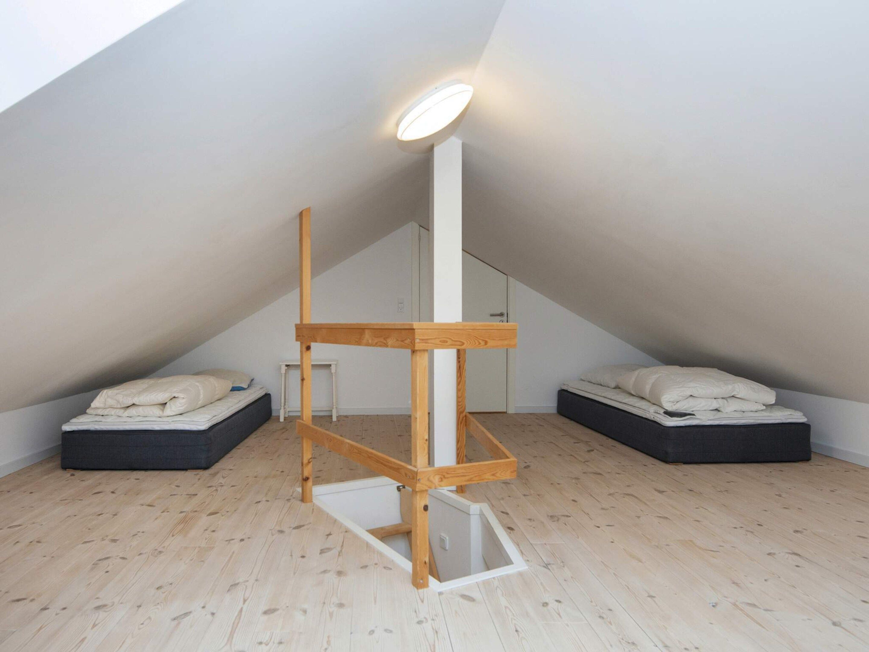 Et værelse med skråvægge, en trækonstruktion i midten, to senge med puder og en lampe i loftet.