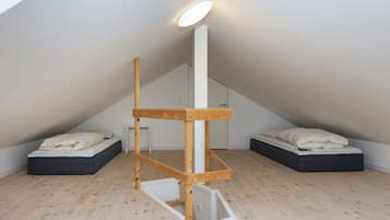 Et værelse med skråvægge, en trækonstruktion i midten, to senge med puder og en lampe i loftet.