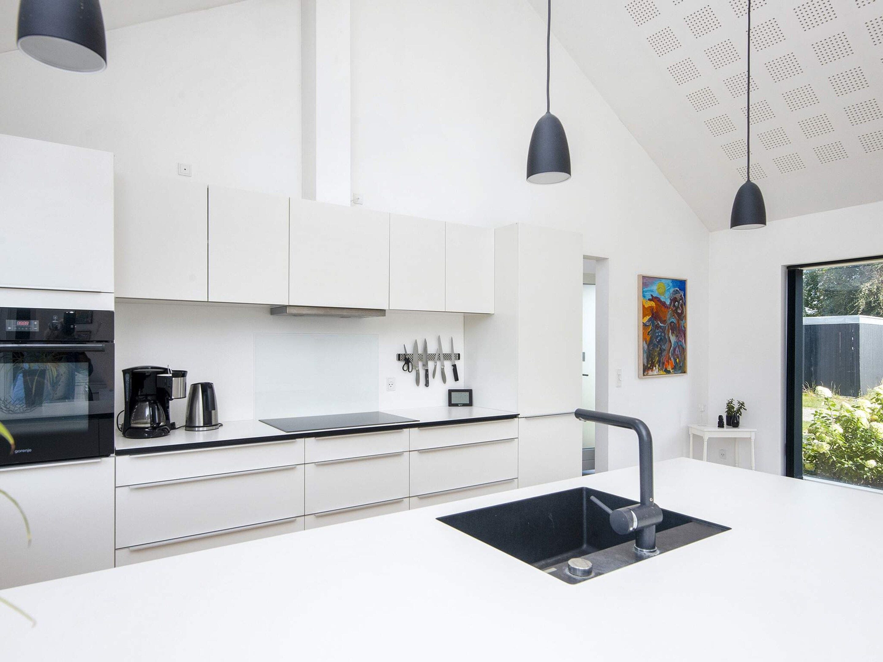 A modern kitchen with white cabinetry, a black countertop, and a black sink. There are two pendant lights, a coffee maker, and a knife block on the counter.