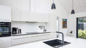 Una cocina moderna con gabinetes blancos, encimera y pileta negra. Hay dos lámparas colgantes, una cafetera y un bloque para cuchillos sobre la encimera.