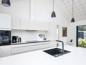 Una cucina moderna con mobili bianchi, un piano di lavoro nero e un lavello nero. Sono presenti luci a sospensione e un quadro appeso al muro.