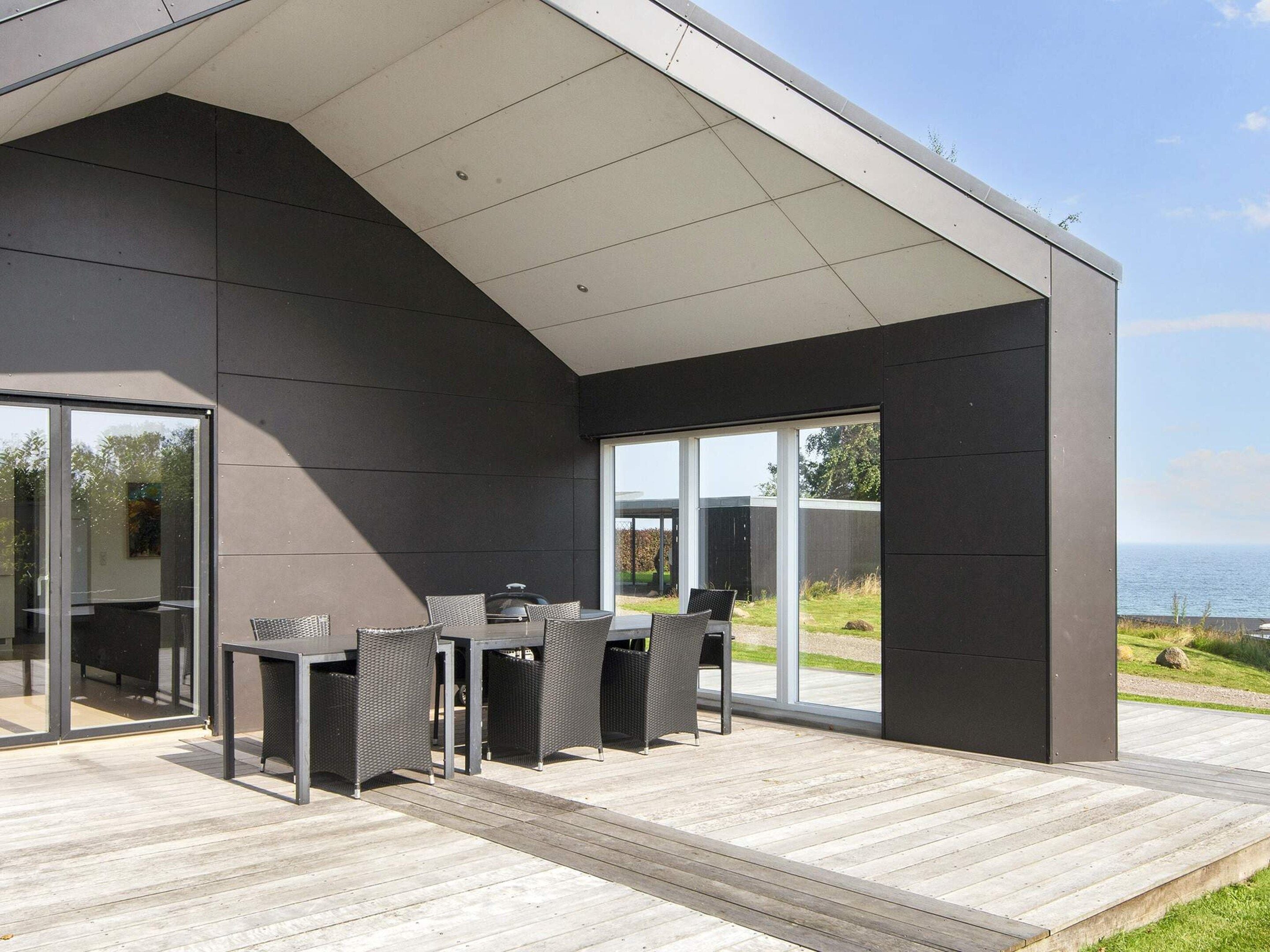 Patio esterno moderno con tavolo da pranzo e barbecue, affacciato su un paesaggio costiero.