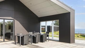 A modern outdoor patio with a dining set and a grill, overlooking a coastal landscape.