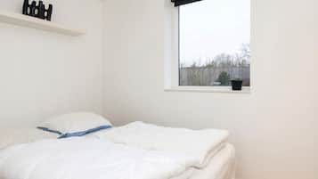 A bedroom with a bed, a window, a shelf with decorative items, and a view of the outside.