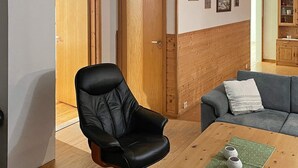 Et værelse med trægulv, en sort læderstol, en grå sofa og et træskab.