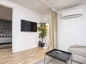 A modern living room with a flat-screen TV, a potted plant, a floor lamp, a sofa, a coffee table, and an air conditioning unit. - 4 Star Holiday Home in Ebeltoft (Ebeltoft)