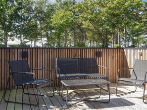 A wooden deck with outdoor furniture, including chairs and a table, surrounded by a wooden fence and trees. - 4 Star Holiday Home in Ebeltoft (Ebeltoft)