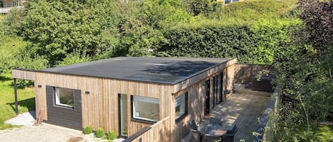 Una casa moderna de madera con techo plano, ventanas amplias y una terraza con mobiliario exterior.
