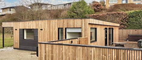 A modern wooden structure with large windows, a door, and a small outdoor seating area.