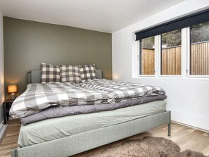 A bed with a checkered bedspread, a nightstand with a lamp, and a window with a view of a fence. - 4 Star Holiday Home in Ebeltoft (Ebeltoft)