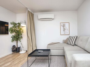 Un salon moderne comprenant un canapé, une table basse, une plante en pot, une lampe et un appareil de climatisation.