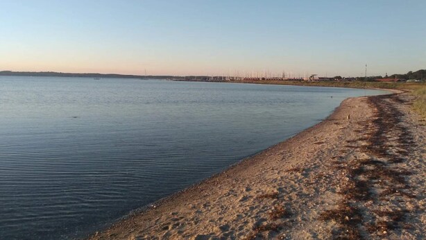 A calm body of water with a sandy shore and distant buildings. - 4 Star Holiday Home in Ebeltoft (Ebeltoft)