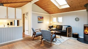 A cozy cabin interior with a wooden ceiling, a dining area with a table and chairs, a living room with a sofa and a fireplace. - 6 Person Holiday Home in Jerup (Jerup)
