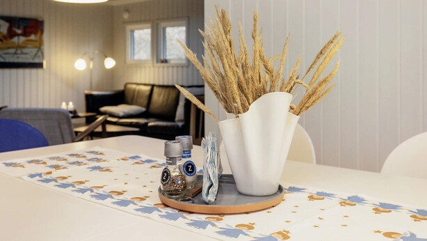 A dining area with a table set for two, featuring a white tablecloth with star patterns, a white vase with dried wheat stalks, and two salt and pepper shakers. - 6 Person Holiday Home in Jerup (Jerup)