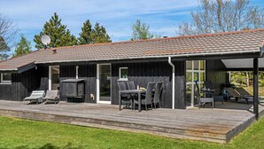 A modern outdoor deck with a dining area, a grill, and lounge chairs. - 6 Person Holiday Home in Jerup (Jerup)