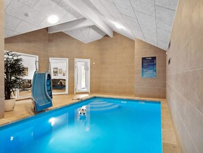 An indoor swimming pool with a slide, a potted plant, and a view of a living room through a glass door. - 5 Star Holiday Home in Henne (Henne)