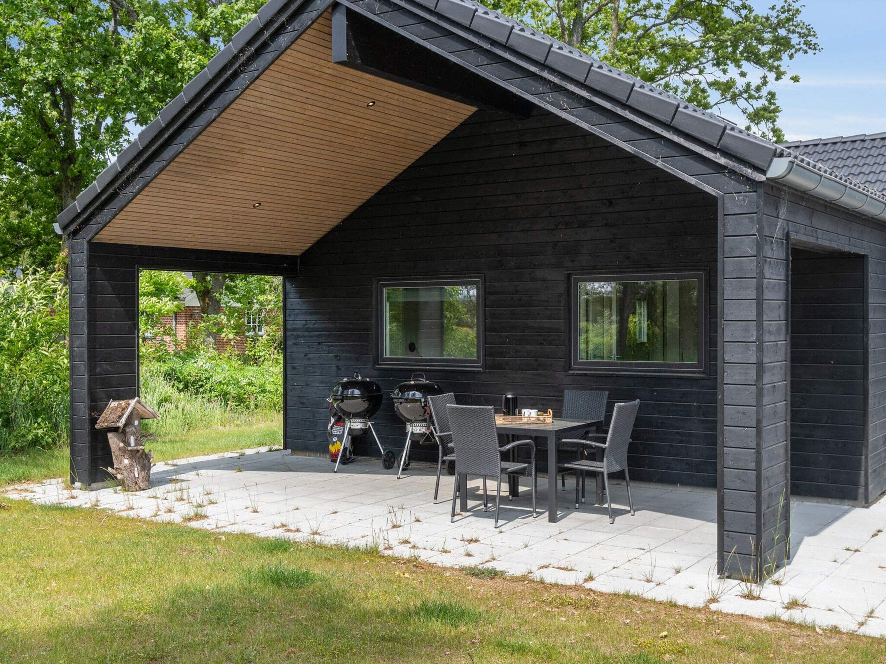 A covered outdoor area with a table and chairs, two barbecue grills, and a bird feeder.