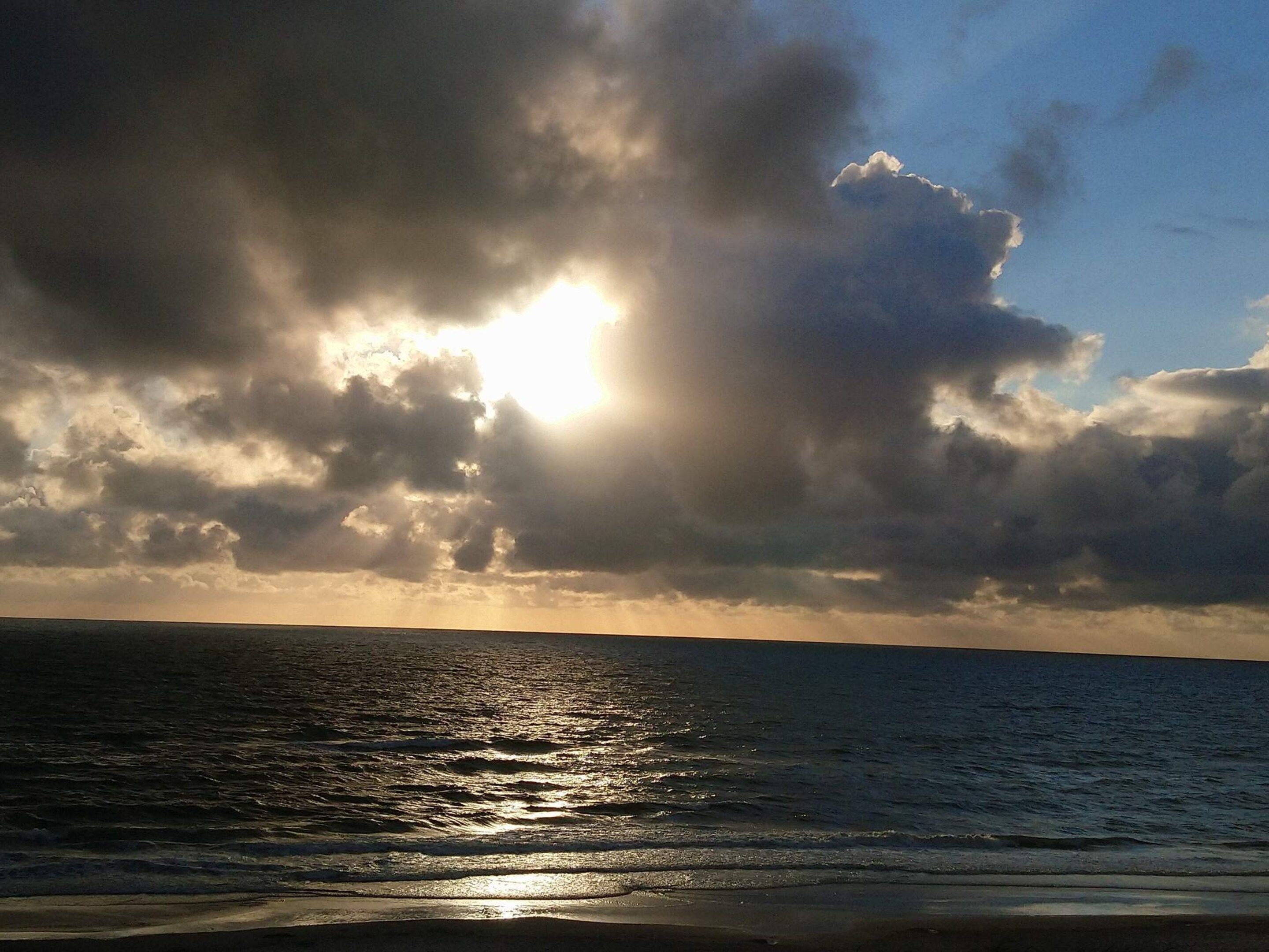 Een strand met de oceaan en een bewolkte lucht.