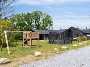 A playground with a swing set and a trampoline, surrounded by a gravel path and large rocks. - 5 Star Holiday Home in Henne (Henne)