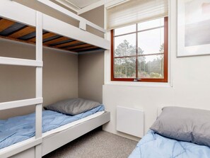 Une chambre de dortoir avec des lits superposés, une fenêtre donnant sur des arbres et un radiateur.