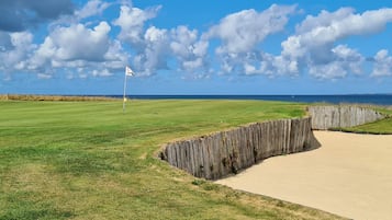 Un campo de golf con una bandera, búnkeres de arena y vista al océano.
