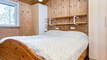 Un dormitorio de madera con una cama, una ventana y estanterías empotradas.